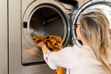 Mature woman placing orange laundry into a large front-loading washing machine