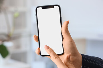 Young woman pointing at mobile phone with blank screen in office