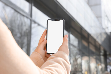 Young woman holding mobile phone with blank screen in city street
