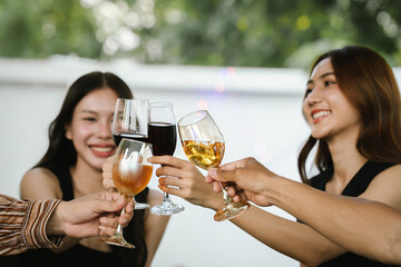Friends clinking glasses of red and white wine in a cheerful toast, smiling and celebrating together in a joyful outdoor gathering.