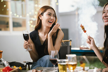 Two young women enjoying grilled food and wine together at an outdoor party, smiling and chatting in a relaxed, friendly atmosphere.