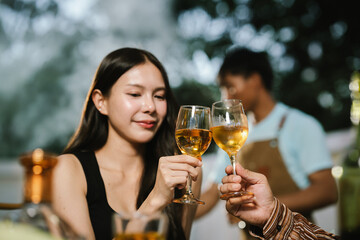 Two young women enjoying grilled food and wine together at an outdoor party, smiling and chatting in a relaxed, friendly atmosphere.