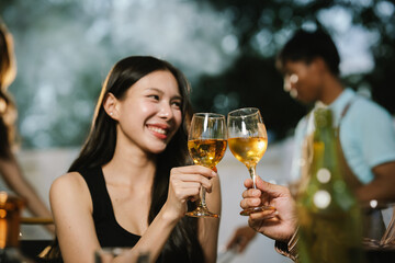 Two young women enjoying grilled food and wine together at an outdoor party, smiling and chatting in a relaxed, friendly atmosphere.