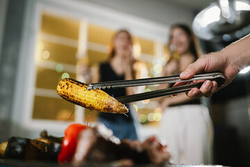 Two young women enjoying grilled food and wine together at an outdoor party, smiling and chatting in a relaxed, friendly atmosphere.
