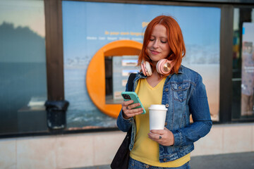 Young woman checking smartphone for mobile banking while holding coffee cup near a financial institution