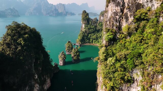 Aerial view of cheow lan lake, Thailand with picturesque landscape of khao sok national park with traditional longtail boat cruising on turquoise water by limestone mountains. 