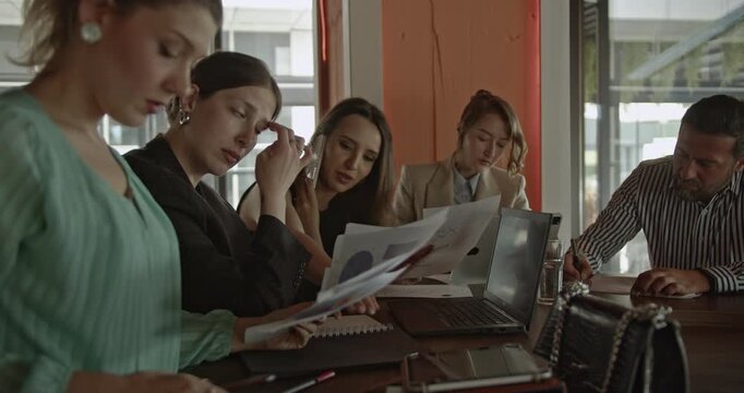 A diverse team of business professionals gathers for a collaborative meeting in a modern office environment. They are actively engaged, discussing ideas, analyzing documents, and working together.