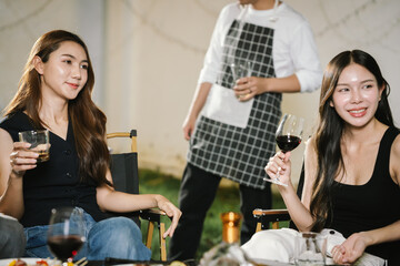 Group of friends enjoying barbecue and wine together in a cozy outdoor party, smiling and chatting in a cheerful atmosphere.
