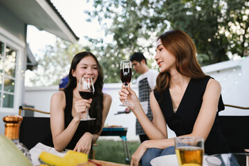 Group of friends enjoying barbecue and wine together in a cozy outdoor party, smiling and chatting in a cheerful atmosphere.
