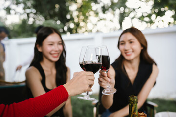Group of friends enjoying barbecue and wine together in a cozy outdoor party, smiling and chatting in a cheerful atmosphere.