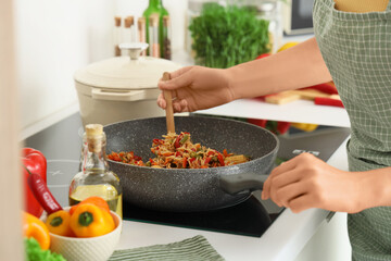 Young woman frying rice with vegetables in kitchen, closeup