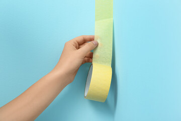 Woman applying masking tape to blue wall, closeup