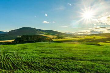 valley view in a green shiny field with green grass and golden sun rays, deep blue cloudy sky on a background , green rural hills in spring young season