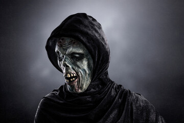 Portrait of a zombie with hooded cape over dark misty background