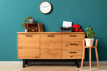 Vintage typewriter, telephone and radio receiver on wooden chest of drawers in interior of living room