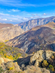Scenic view of a deep mountain gorge with autumn trees and rocky cliffs under a blue sky.