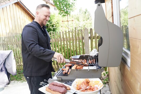 man grilling barbecue meat in backyard at home