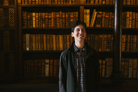 Young adult man smiling in front of book shelf in library