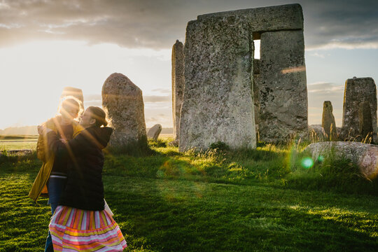 Tween girls dance in sun rays next to Stonehenge in green grass