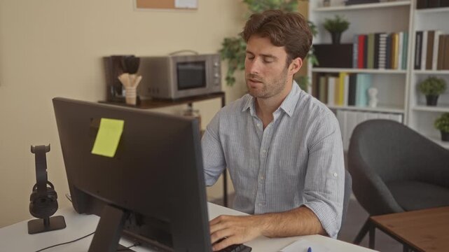 Man typing on keyboard at computer desk in building office, leaning forward with head bowed over the monitor and resting on forearm; tiredness focus.