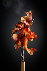 Fried bacon with rosemary on a fork.