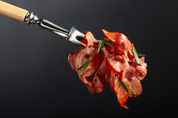 Fried bacon slices with rosemary on a fork.