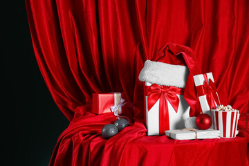 Beautiful gift boxes with letters to Santa, cup of cacao and Christmas balls near red curtain on...