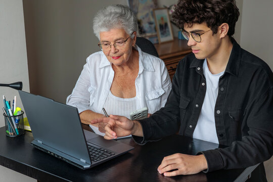 Teenage grandson teaching his grandmother to use a laptop at home. Generations learning together, family support, digital literacy for seniors, technology, connection, love, and intergenerational care - Powered by Adobe