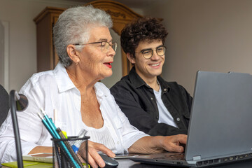 Teenage grandson teaching his grandmother to use a laptop at home. Generations learning together, family support, digital literacy for seniors, technology, connection, love, and intergenerational care