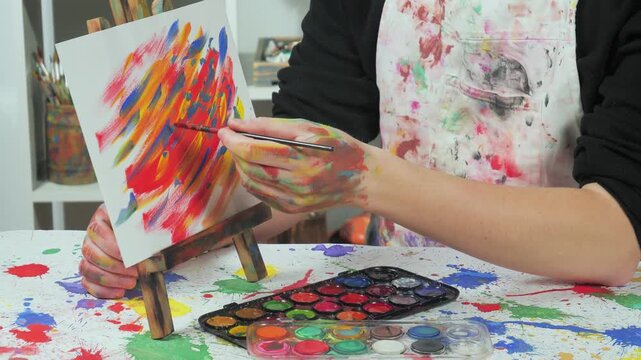 The hands of the artist, work to create creative images in art. Art paints and brushes, applying multi-coloured strokes to the canvas using palette, gouache and watercolour.