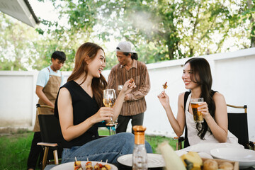 Group of friends enjoying barbecue and wine together in a cozy outdoor party, smiling and chatting in a cheerful atmosphere.