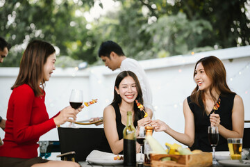 Group of friends enjoying barbecue and wine together in a cozy outdoor party, smiling and chatting in a cheerful atmosphere.