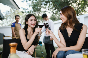 Group of friends enjoying barbecue and wine together in a cozy outdoor party, smiling and chatting in a cheerful atmosphere.