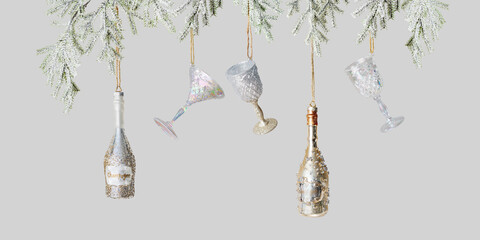 Shiny Glass of wine and Champagne bottle Christmas ornaments hang on fir tree branch. New Year gold silver toys as wineglass and sparkling wine. Winter holiday minimal banner, festive drink concept.