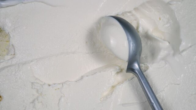 Scoops of vanilla ice cream are slowly placed on a spoon and removed from the container.