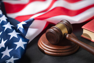 A judge gavel on sound block with Law book and American flag on a black surface, symbolizing...