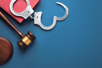 Judge gavel, handcuffs and Law book on a blue surface.