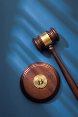 Judge gavel and a Bitcoin coin on sound block set against a blue background with soft lighting. Top view, flat lay.