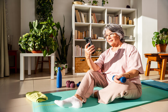 Senior Woman Follows Exercise Routine at Home Using Phone in Bright Living Room
