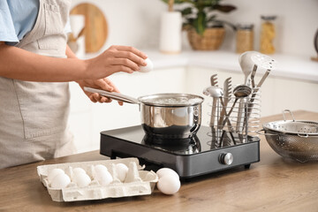 Woman putting egg into saucepan with boiling water in kitchen