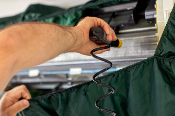 male hand of worker from the cleaning service cleans the air conditioner by spraying water, close-up
