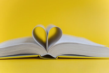 An open book with heart-shaped pages on a bright yellow background. Book Lovers Day. Poetry Day. Knowledge Day. Back to School Minimalism Concept. Authors Day. Space for text. Space for copying