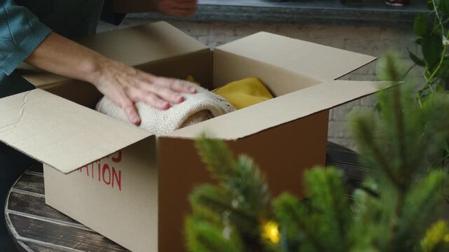 Christmas donation, charity concept. Woman packing clothes in donation box.