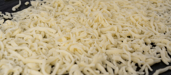 Grated mozzarella cheese on black background. Shredded mozarella texture