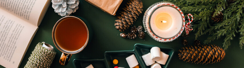 Cozy winter scene with a cup of tea, candle, and festive decorations.