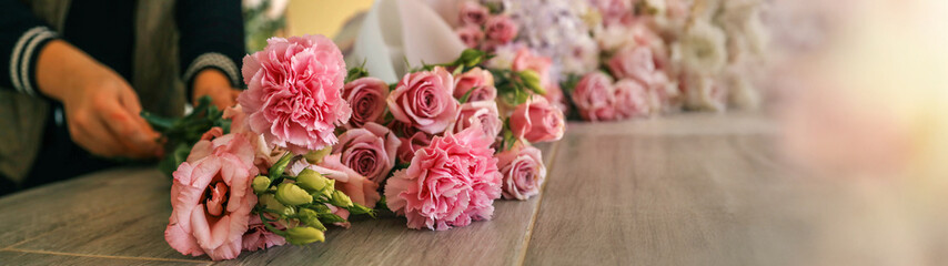 Florist arranging a bouquet of pink flowers on a wooden table