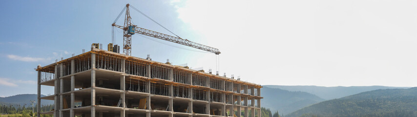 Construction site with a crane against a blue sky and mountains in the background. © shine.graphics