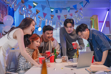 Excited office team celebrates incredible profit growth and victory results announcement together, cheering enthusiastically while monitoring financial performance on screen during triumphant night