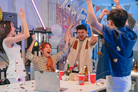 Excited office team celebrates incredible profit growth and victory results announcement together, cheering enthusiastically while monitoring financial performance on screen during triumphant night
