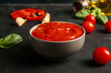 Bowl of tasty tomato sauce with basil leaves on black background, closeup